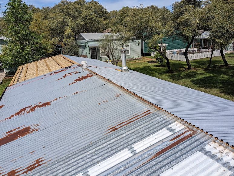 An aerial view of a rusty metal roof with trees in the background.
