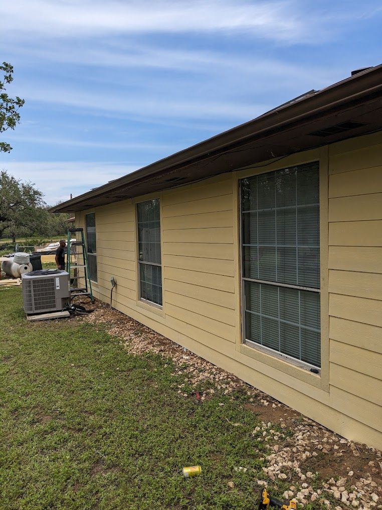 A yellow house with a lot of windows is sitting on top of a lush green field.