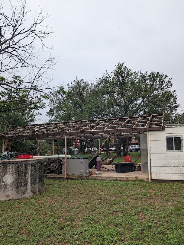 A white house with a wooden roof is sitting in the middle of a grassy field.