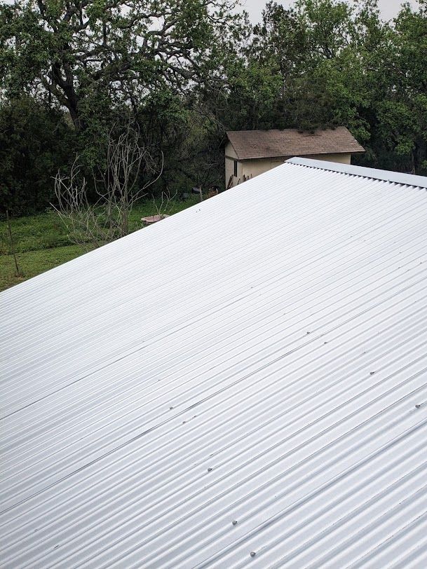 A white metal roof with trees in the background and a house in the background.