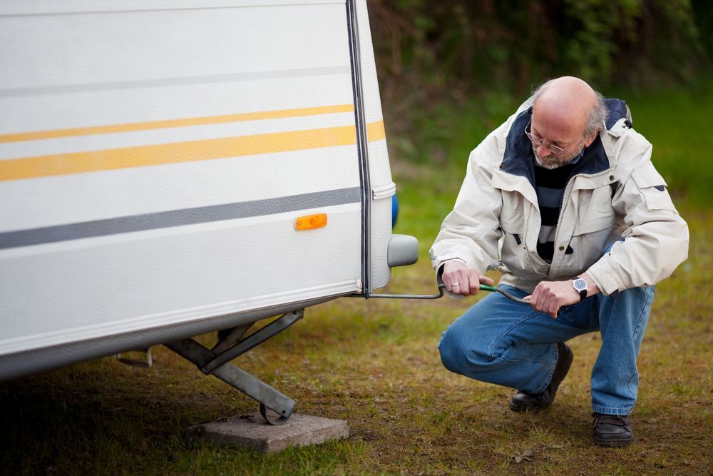A Man Is Kneeling Besides A Caravan Lifting It With A Jack — Kingston Caravan Repairs In Maitland, NSW