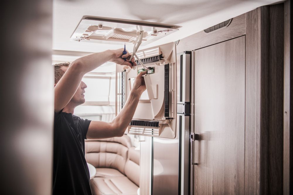 A Man Is Working On A Refrigerator In A Camper — Kingston Caravan Repairs In Heatherbrae, NSW