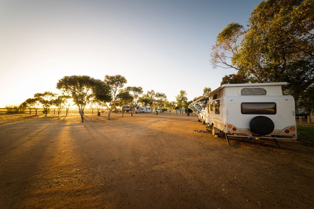 A Caravan Is Parked In A Dirt Lot With Trees In The Background — Kingston Caravan Repairs In Port Stephens, NSW