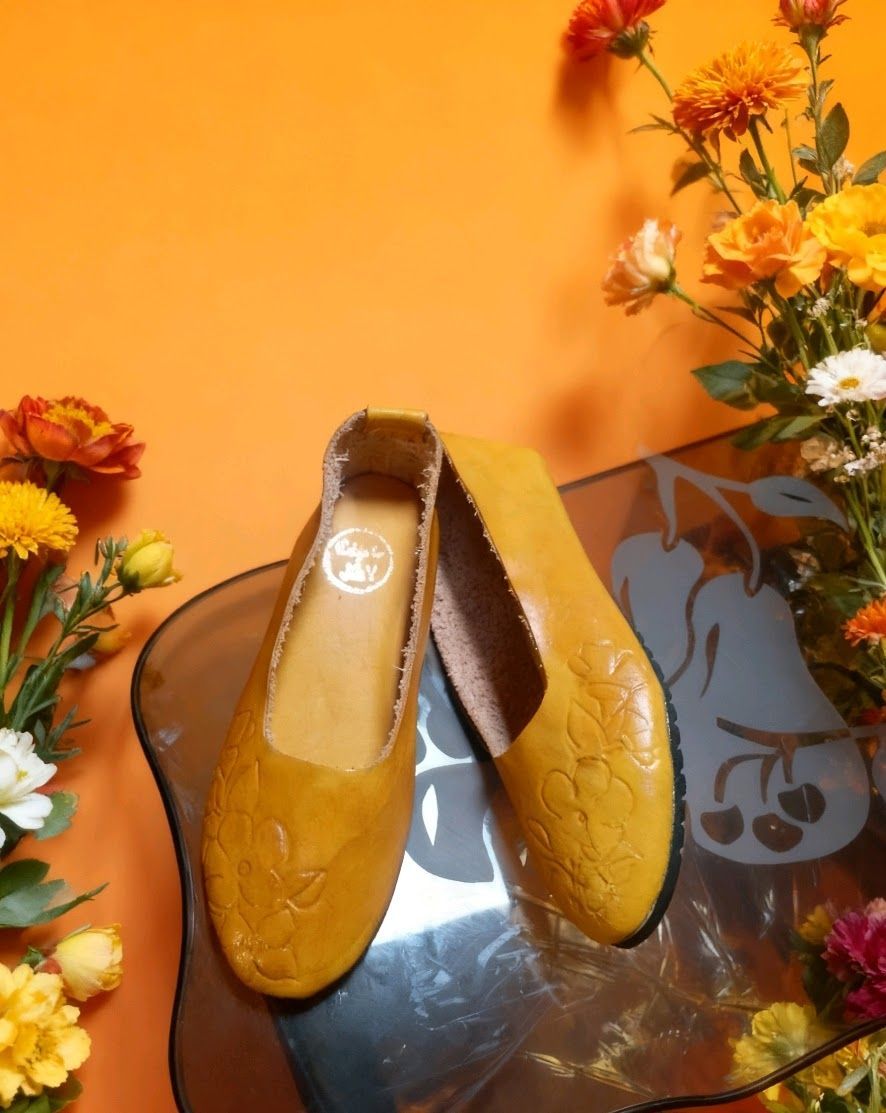 Un par de zapatos sin cordones de cuero amarillo con motivos florales en relieve