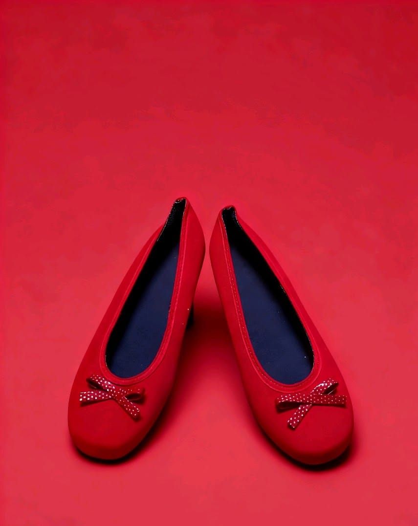 Un par de zapatos planos de color rojo brillante con lazos decorativos en la punta