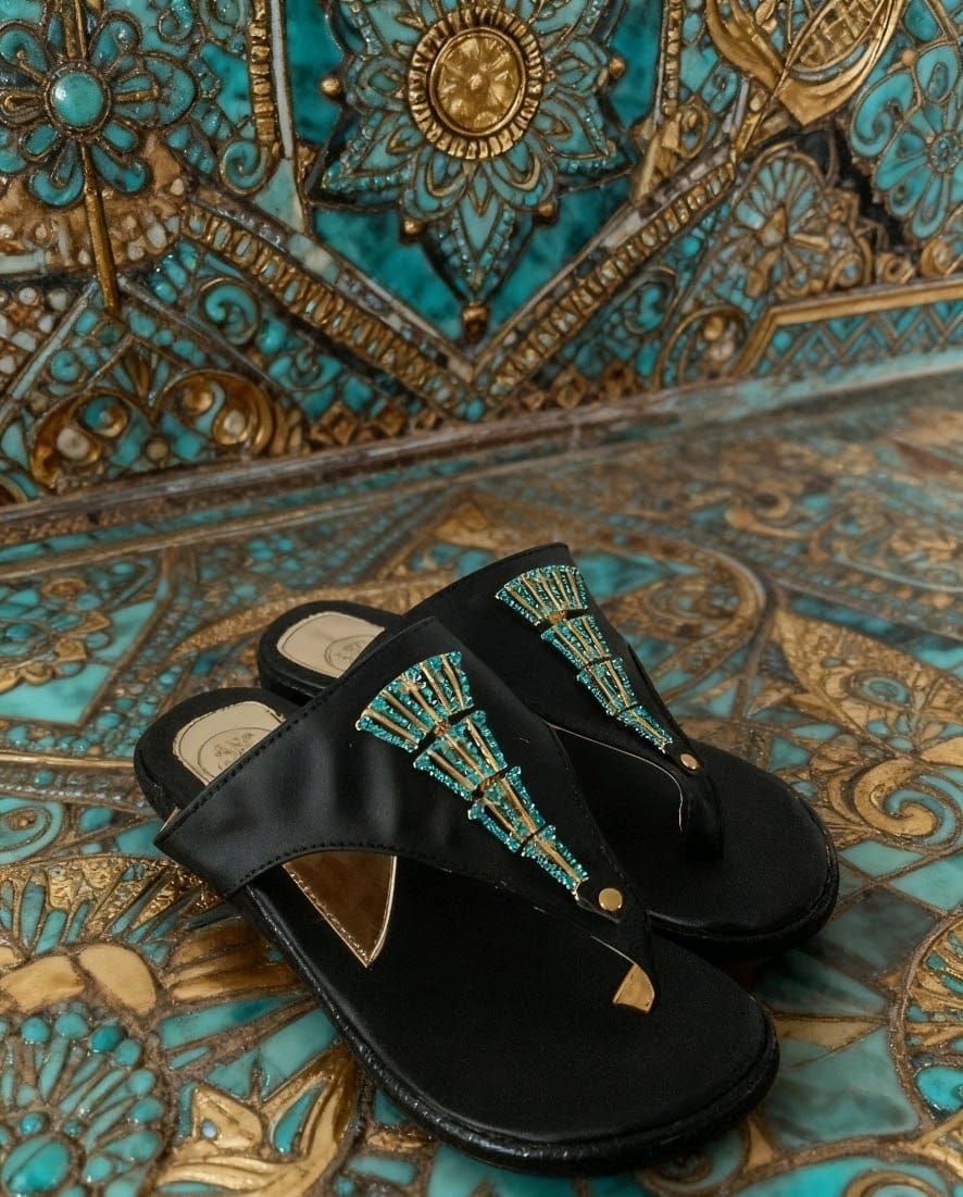 Sandalias negras de dedo decoradas con flecos de color verde azulado sobre una superficie de azulejos 