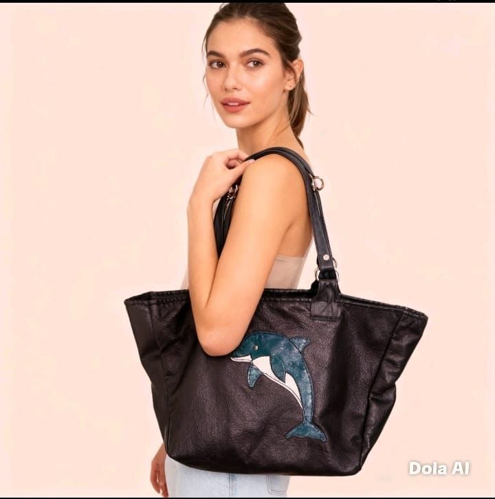 Una persona sostiene una bolsa de tela grande de color negro con un dibujo de un delfín azul sobre un fondo rosa claro.