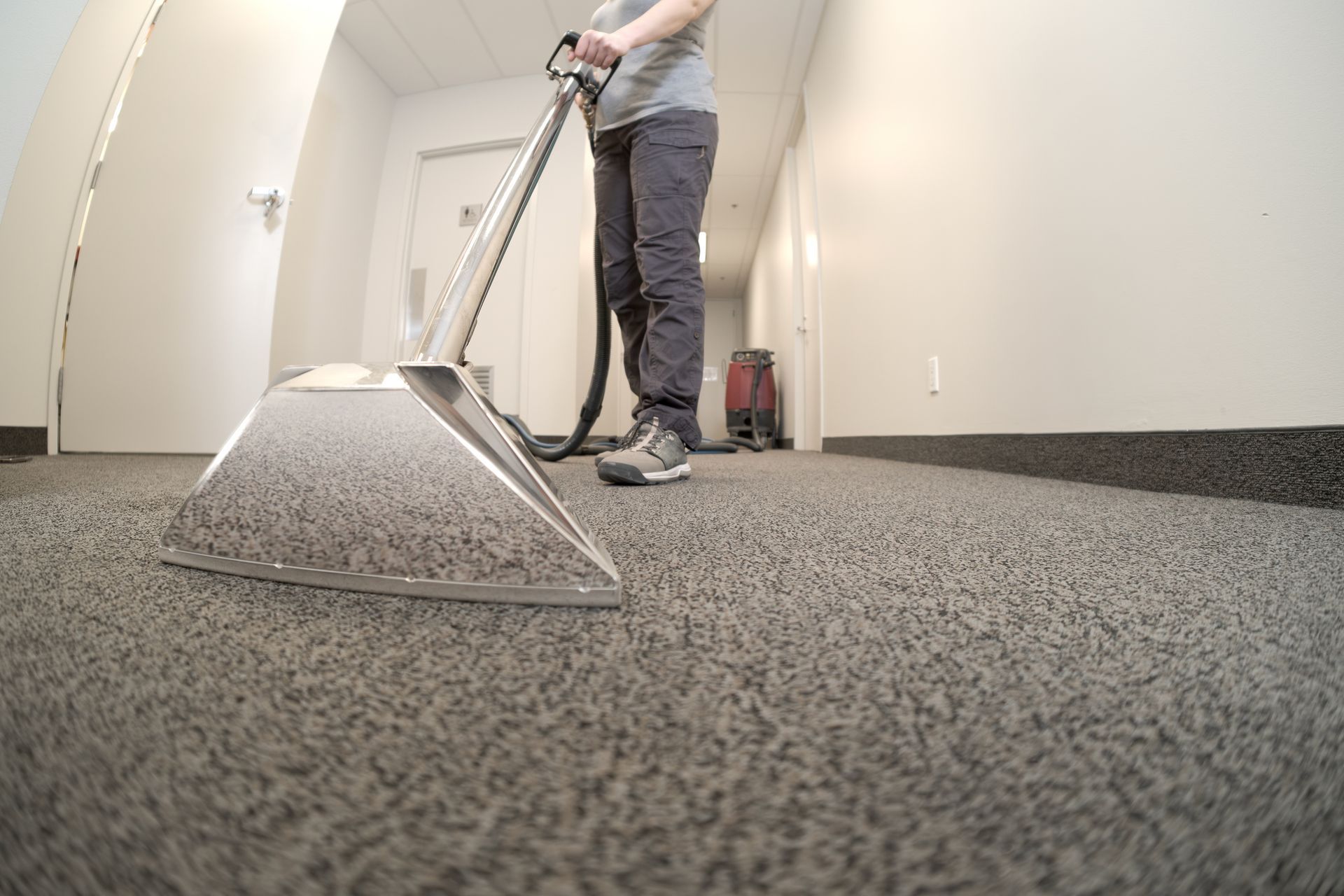 Close-up of steam cleaning machine head during commercial carpet cleaning in modern office hallway.