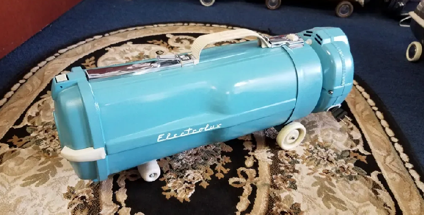 A vintage, bright blue Electrolux canister vacuum cleaner with white wheels, sitting on a patterned rug.
