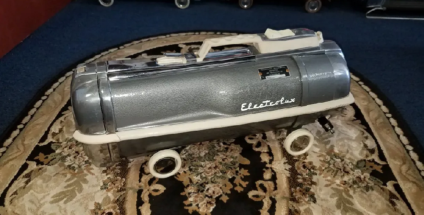 A vintage gray Electrolux canister vacuum cleaner with chrome accents and white wheels, sitting on a patterned rug.