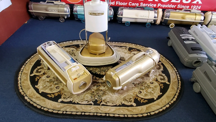 A display of several vintage Aerolux canister vacuum cleaners arranged on a patterned rug in a retail setting.