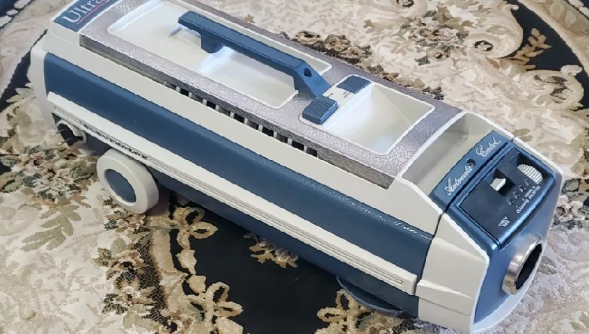 A vintage blue and off-white Kenmore canister vacuum cleaner sits on a patterned rug.