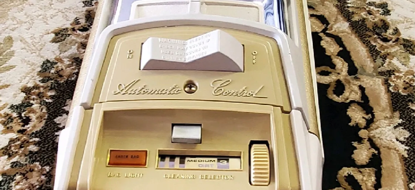 Close-up of a vintage tan Eureka vacuum cleaner control panel with a top power switch and lower speed settings.