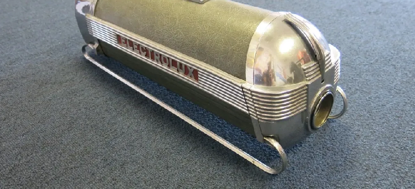 A vintage Electrolux canister vacuum cleaner in olive green and chrome, sitting on a gray carpet.