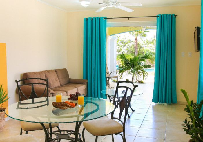 Living room with turquoise curtains, brown sofa, glass table, and open doors to a patio.