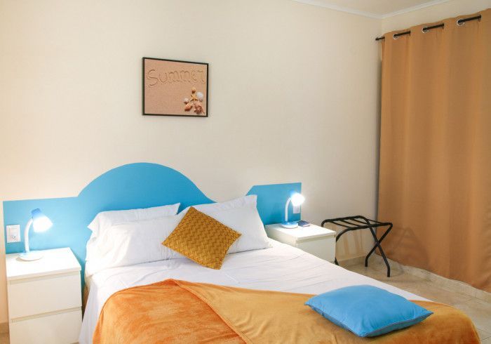 Bedroom with blue headboard, bed, bedside tables, and orange accents.
