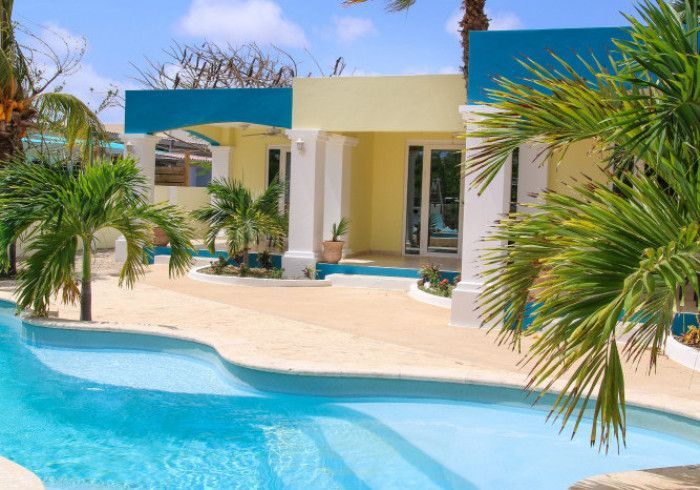 Tropical home with a turquoise pool, palm trees, and yellow and blue facade.
