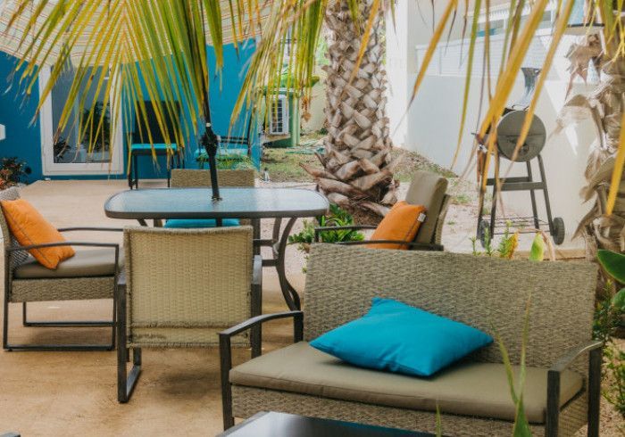 Outdoor patio with seating, table, grill, and palm trees. Orange and blue cushions.