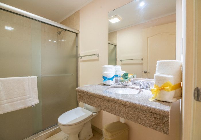 Bathroom with a toilet, sink, shower, and towels. Light beige walls and a granite countertop.