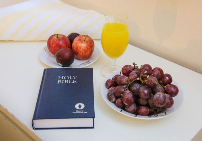A bedside table with a Bible, fruit, and a glass of juice.