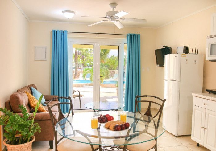 Interior view of a living space with a pool visible through glass doors. Includes dining table, sofa, and kitchen.