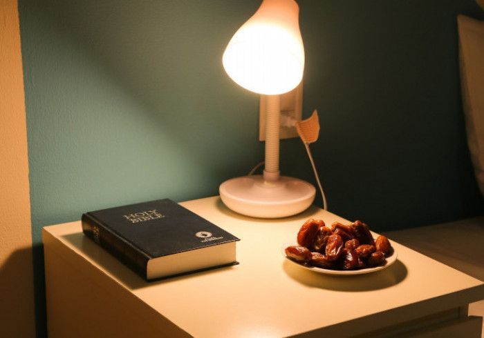 Nightstand with Bible, dates, and lamp illuminated on teal wall.