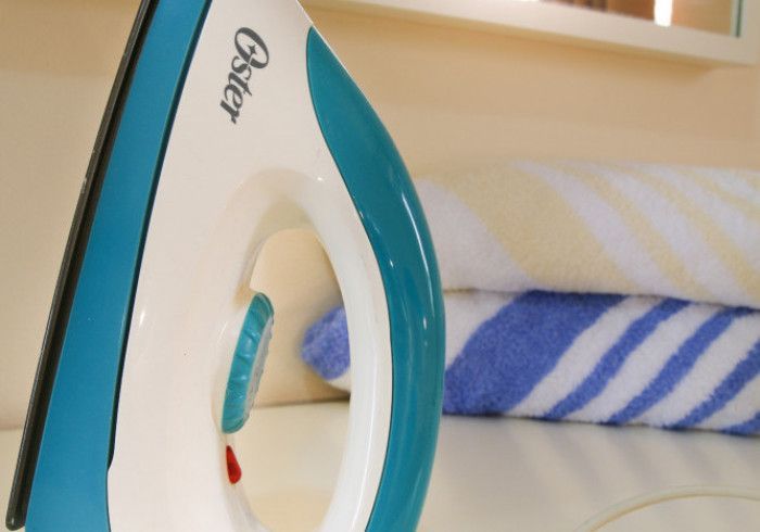 A white and turquoise Oster iron sits on a surface near rolled-up towels.