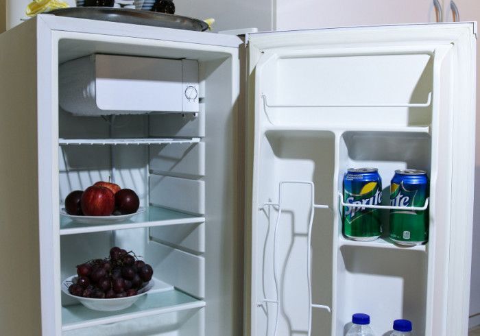 Open mini-fridge with fruit on shelves: apples, grapes, and Sprite cans.