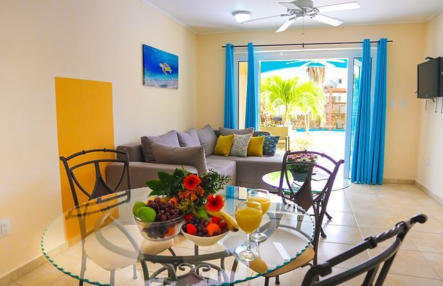 Living room with glass table, sofa, and open door to pool area.