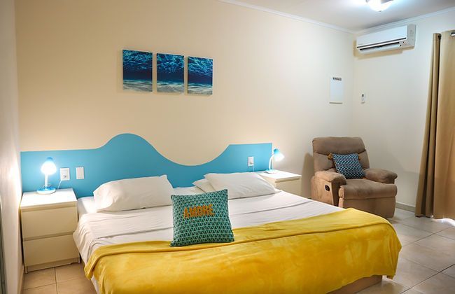 Bedroom with a blue headboard, bed with yellow blanket, white nightstands, and a recliner chair.