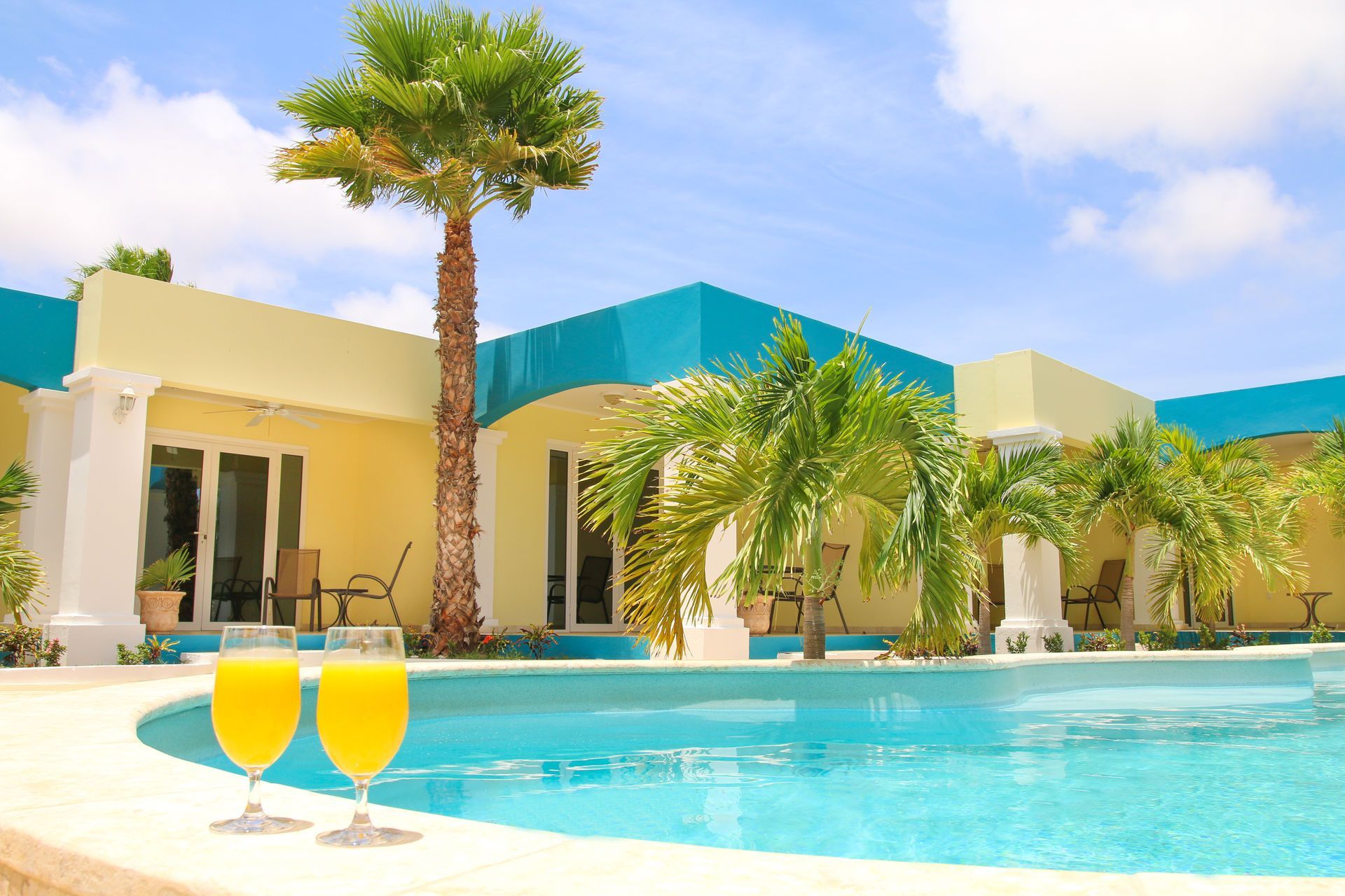 Poolside view: tropical villa with pool, palm trees, and two orange cocktails.