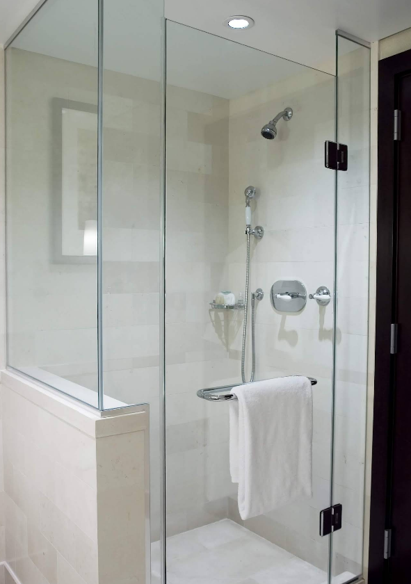 Glass-enclosed shower with a white towel on a towel bar. Light-colored tile walls, showerhead, and a dark door.