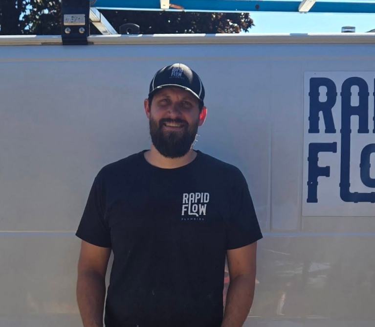 Man in black t-shirt and cap smiles in front of white van with 