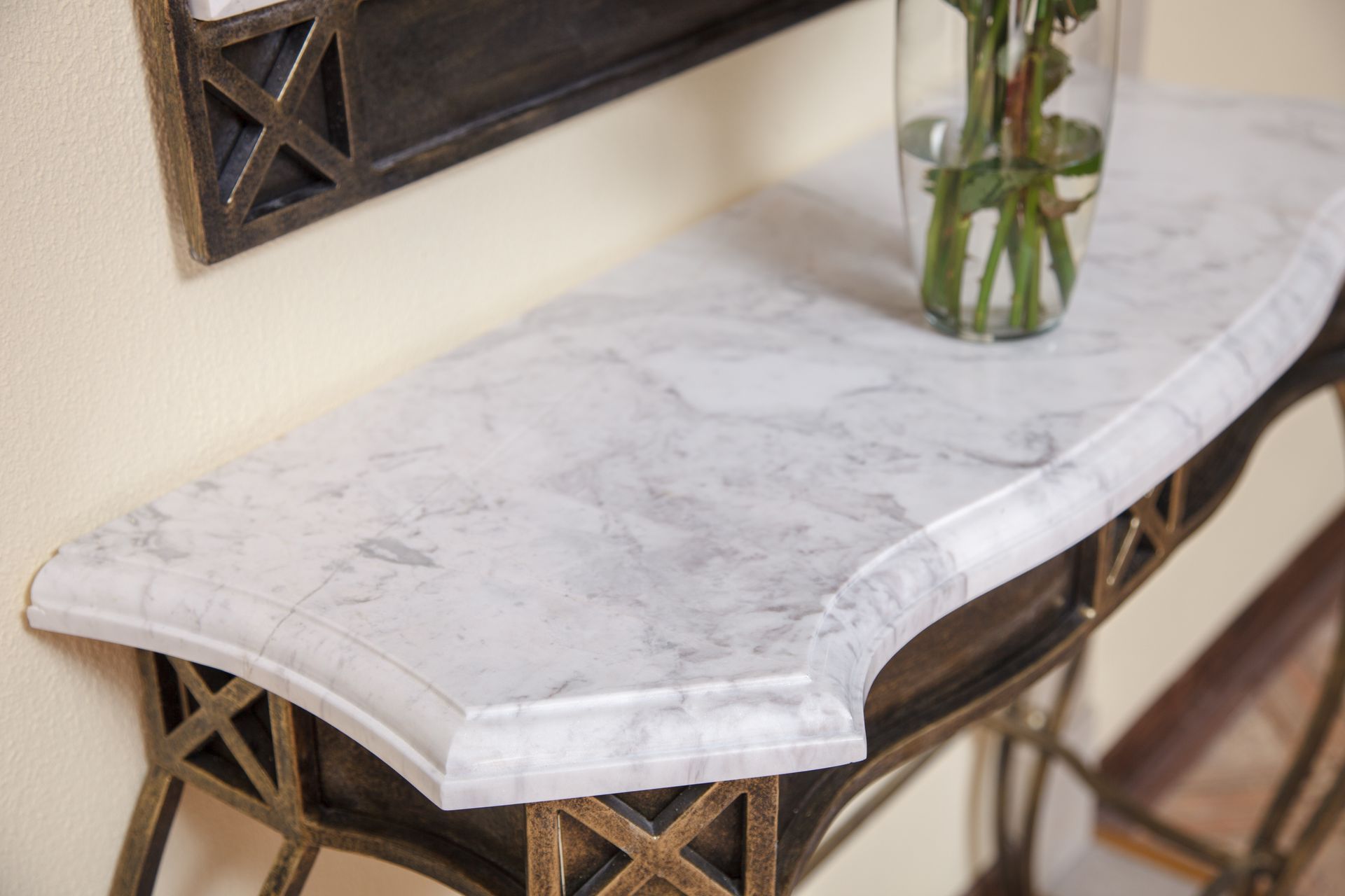 A faux marble console table with a metal lattice base and a glass vase of greenery sitting on top.