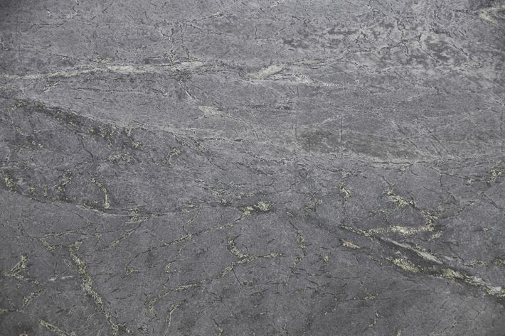 A close-up, top-down view of a textured dark gray stone surface with subtle white and green mineral veining throughout.