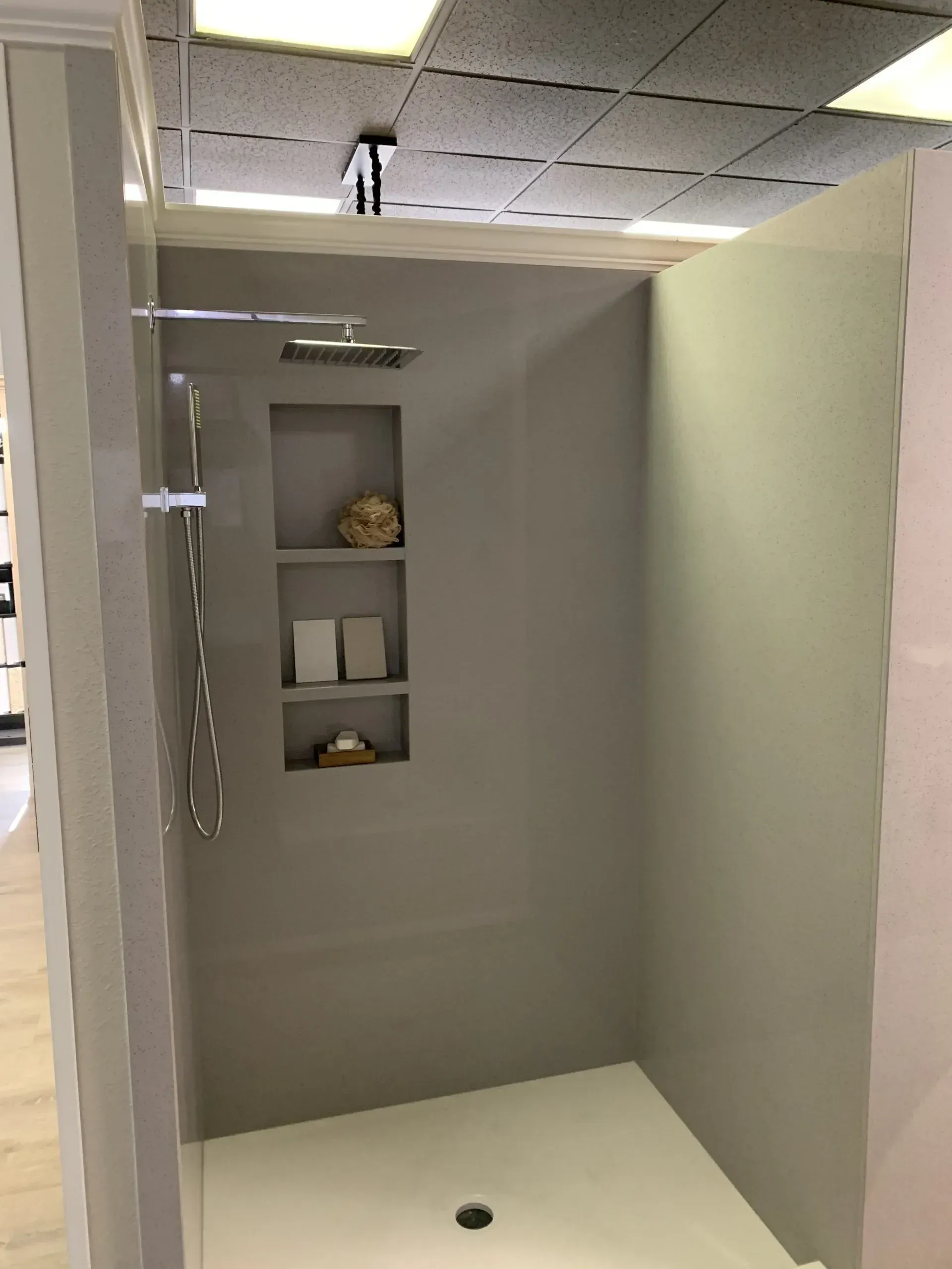 A modern walk-in shower with matte taupe walls, a built-in three-tier niche, a rainfall showerhead, and a white base.