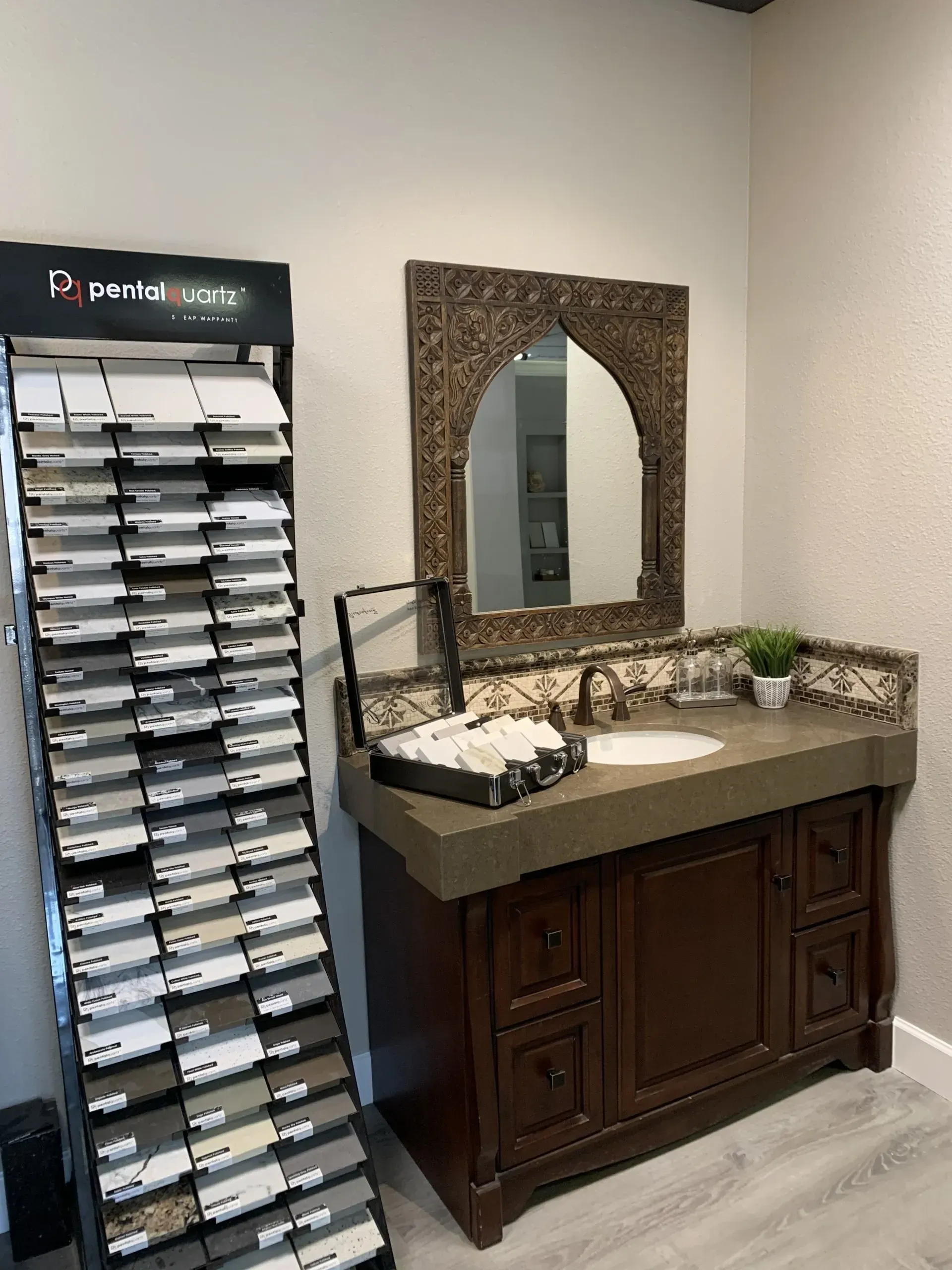 A bathroom vanity display featuring a dark wood cabinet, a concrete countertop, and an arched, ornate mirror.