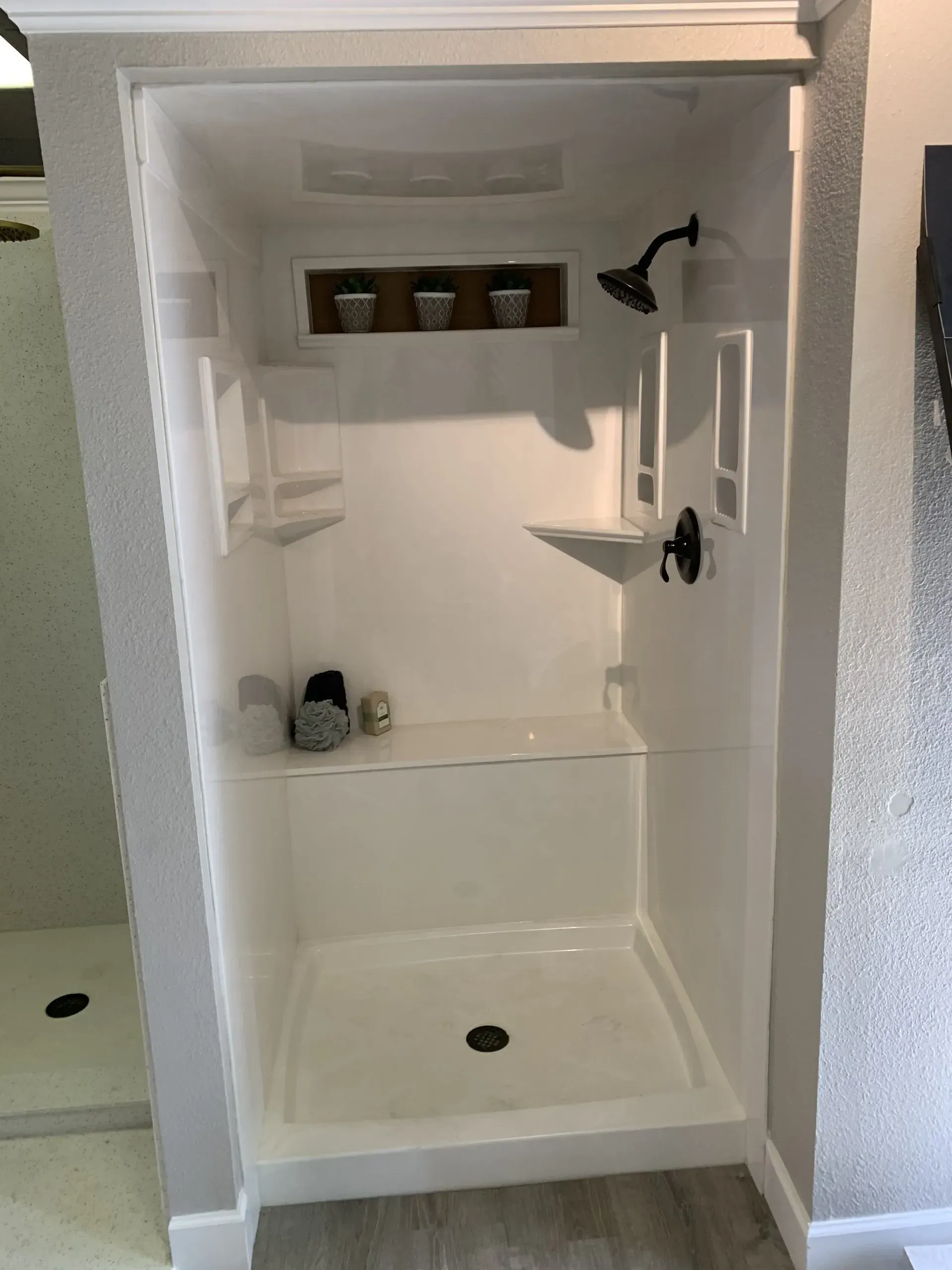 A white walk-in shower with a built-in bench, overhead showerhead, corner shelves, and a decorative recessed niche.