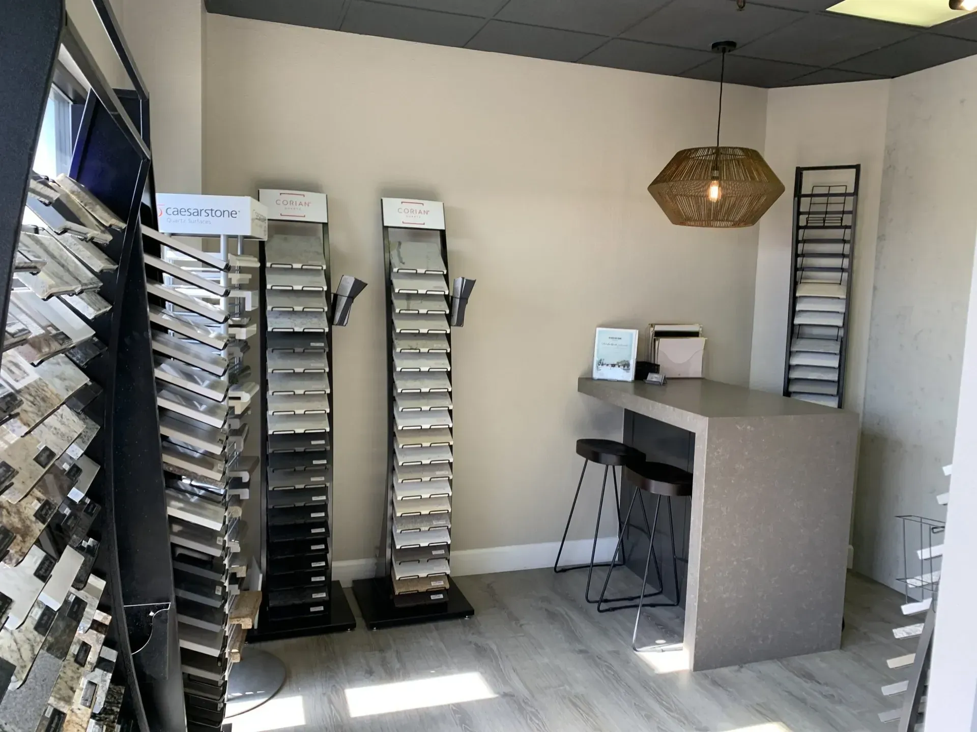 A design showroom with sample racks of stone and tile next to a counter with two stools and a geometric pendant light.