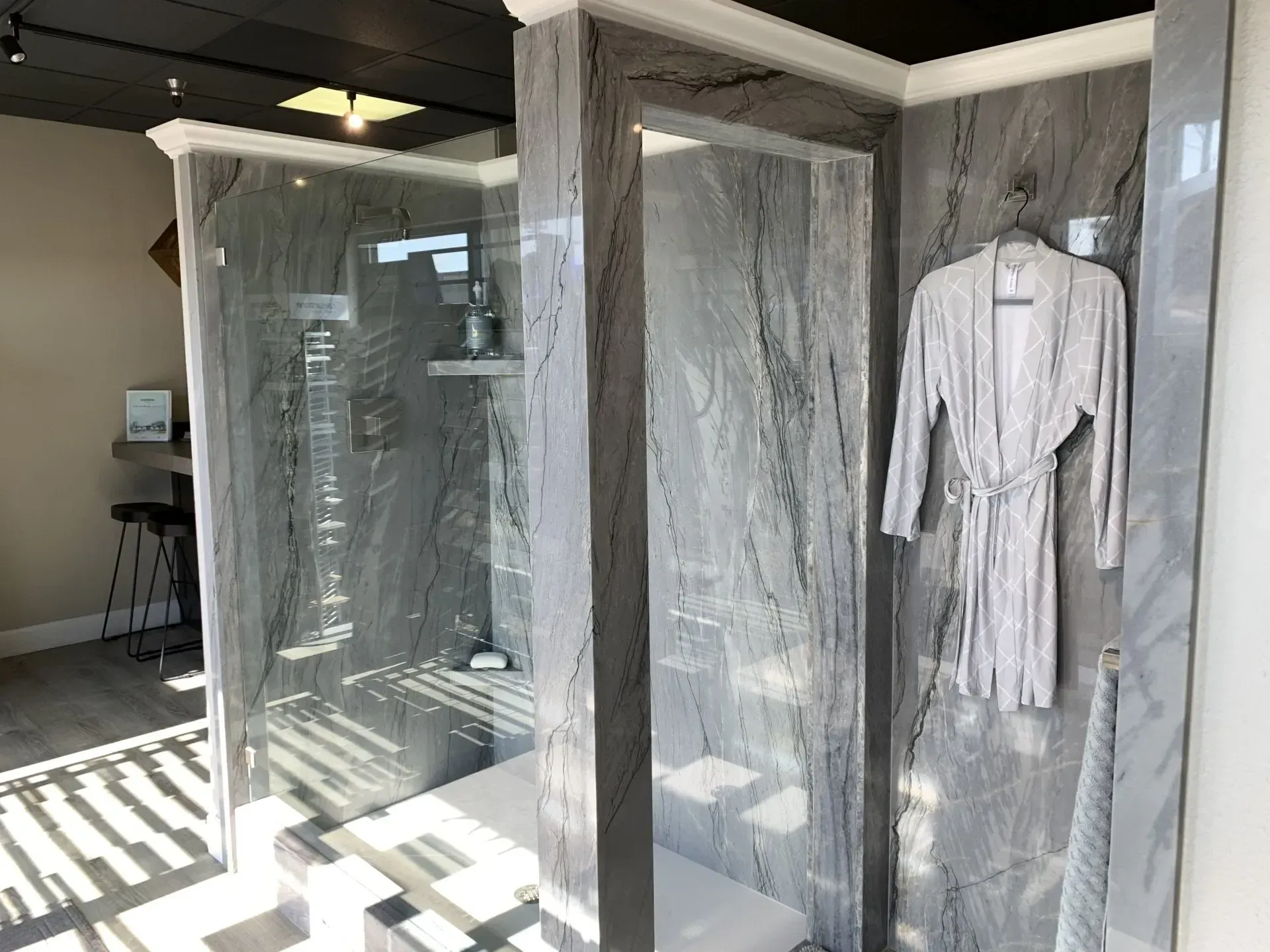 A modern shower enclosure with grey veined stone walls, glass doors, and a robe hanging on the outside wall.