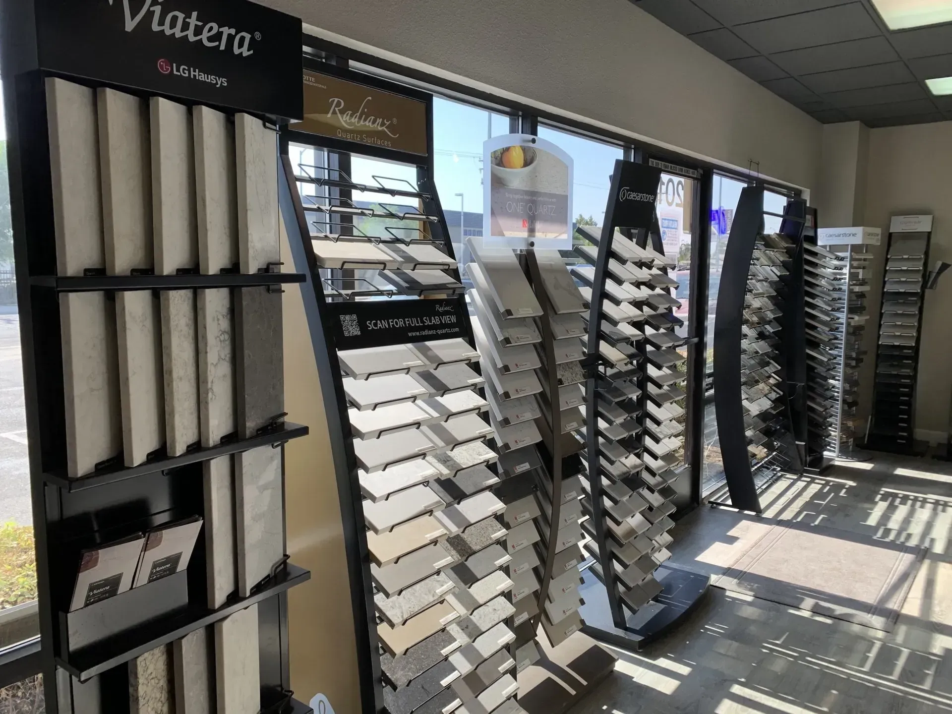 Rows of tall display racks showcasing various stone and tile samples in a showroom with large windows.