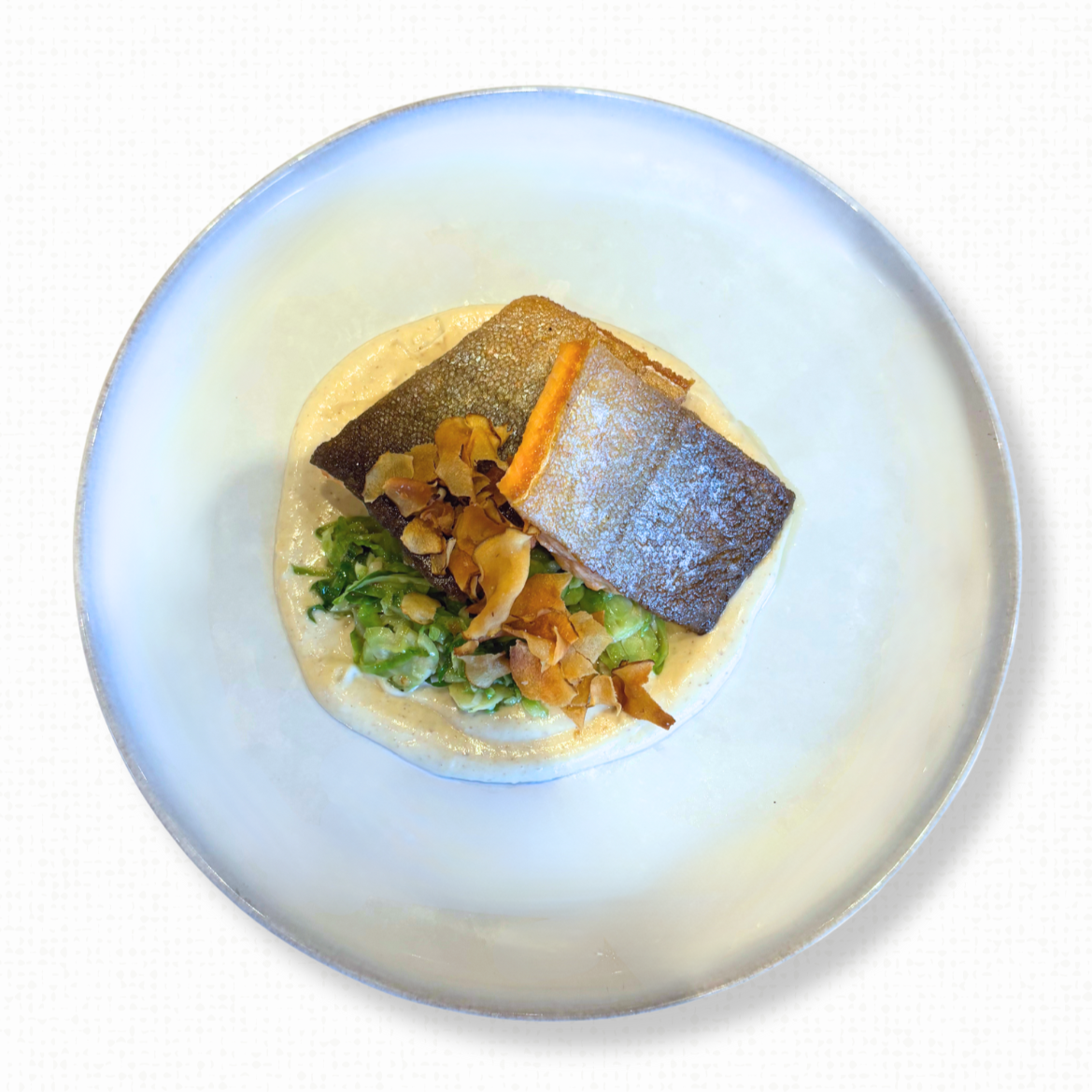 A plate of Arctic Char with Sunchokes & Shaved Brussels Sprouts on a white tablecloth-covered table. 