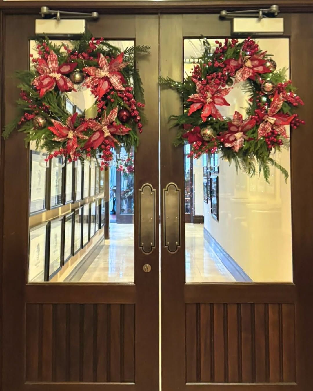 Two Christmas wreaths decorated with red plaid hung on two doors with large windows. 