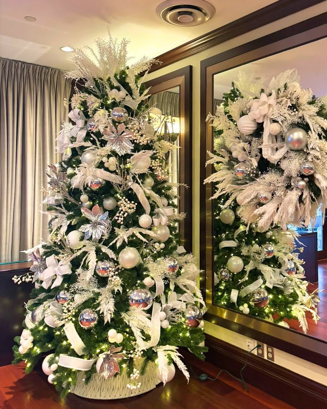 Large Christmas tree and wreath decorated in white and silver in the corner of an event room. 