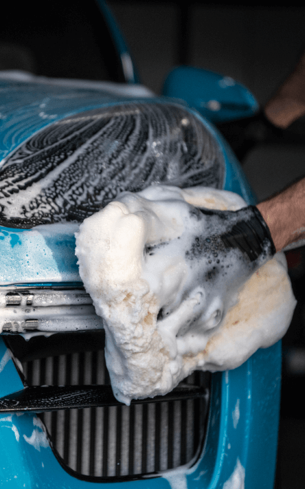 Soap foaming as someone scrubs the headlights of a car