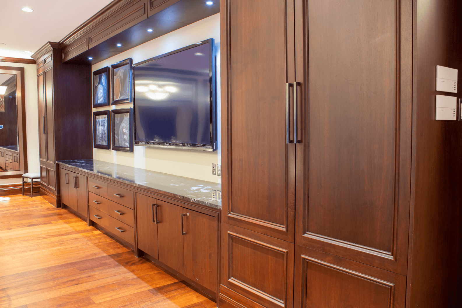 The large TV hung on the wall surrounded by hanging picture frames and cabinetry in the Nest.