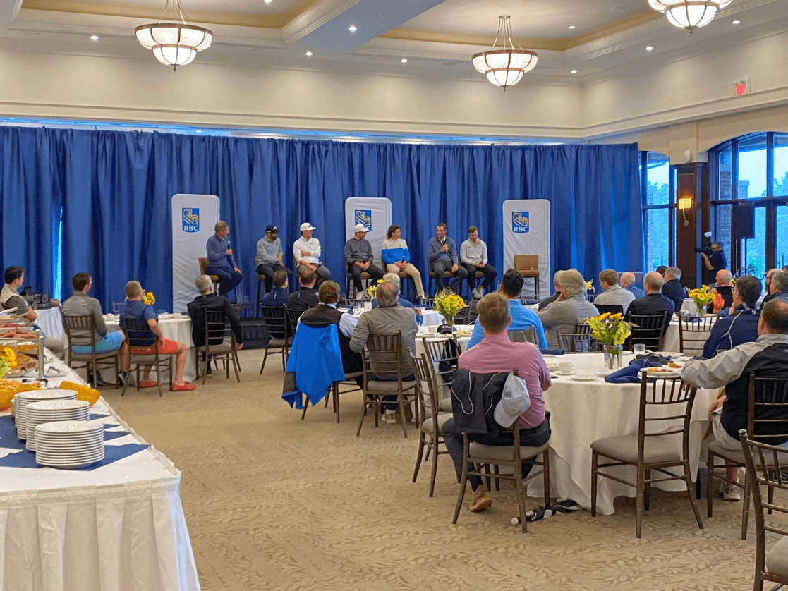 a group of people sit at tables in a room with a blue curtain behind them
