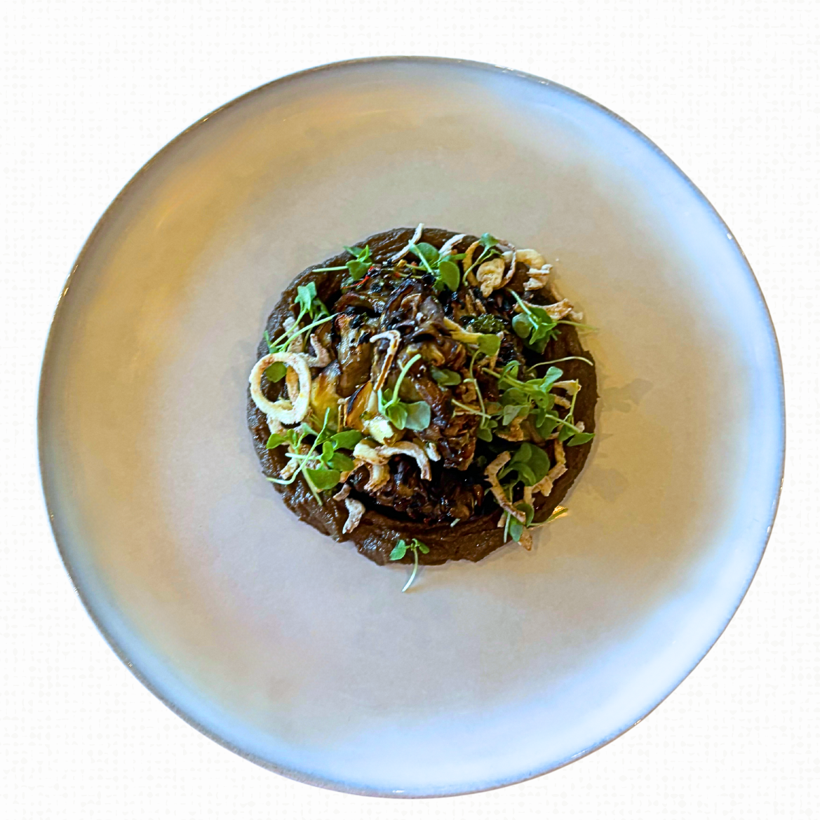 A plate of Hen of the Woods with Mushroom Agrodolce. Gremolata, Fresh Herbs & Crunchy Shallots on a white tablecloth-covered table. 