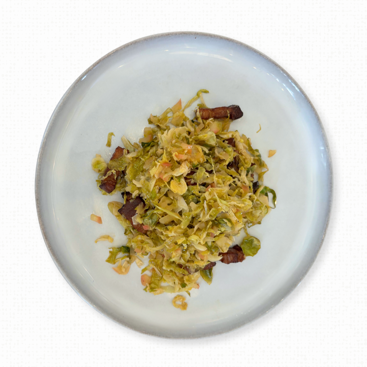 A plate of Shaved Brussels Sprouts
with Apple & Double Smoked Bacon on a white tablecloth-covered table. 