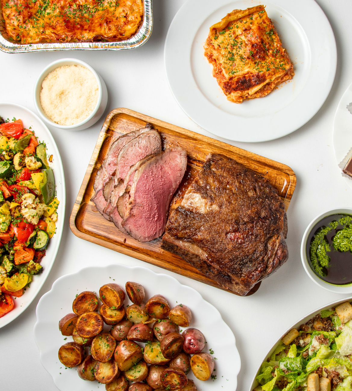 Strip Loin, Lasagna, Potatoes, and Salad on a white tablecloth-covered table.  